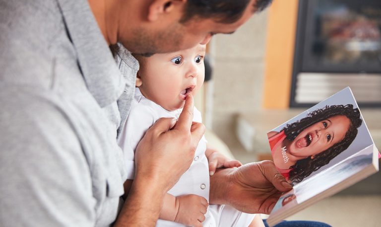 Father reads to his baby while pointing out a body part.