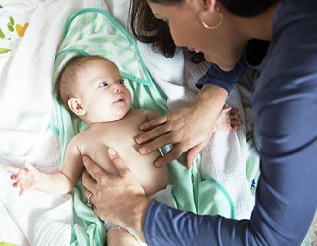 Baby laying on a towel while a woman is touching their stomach