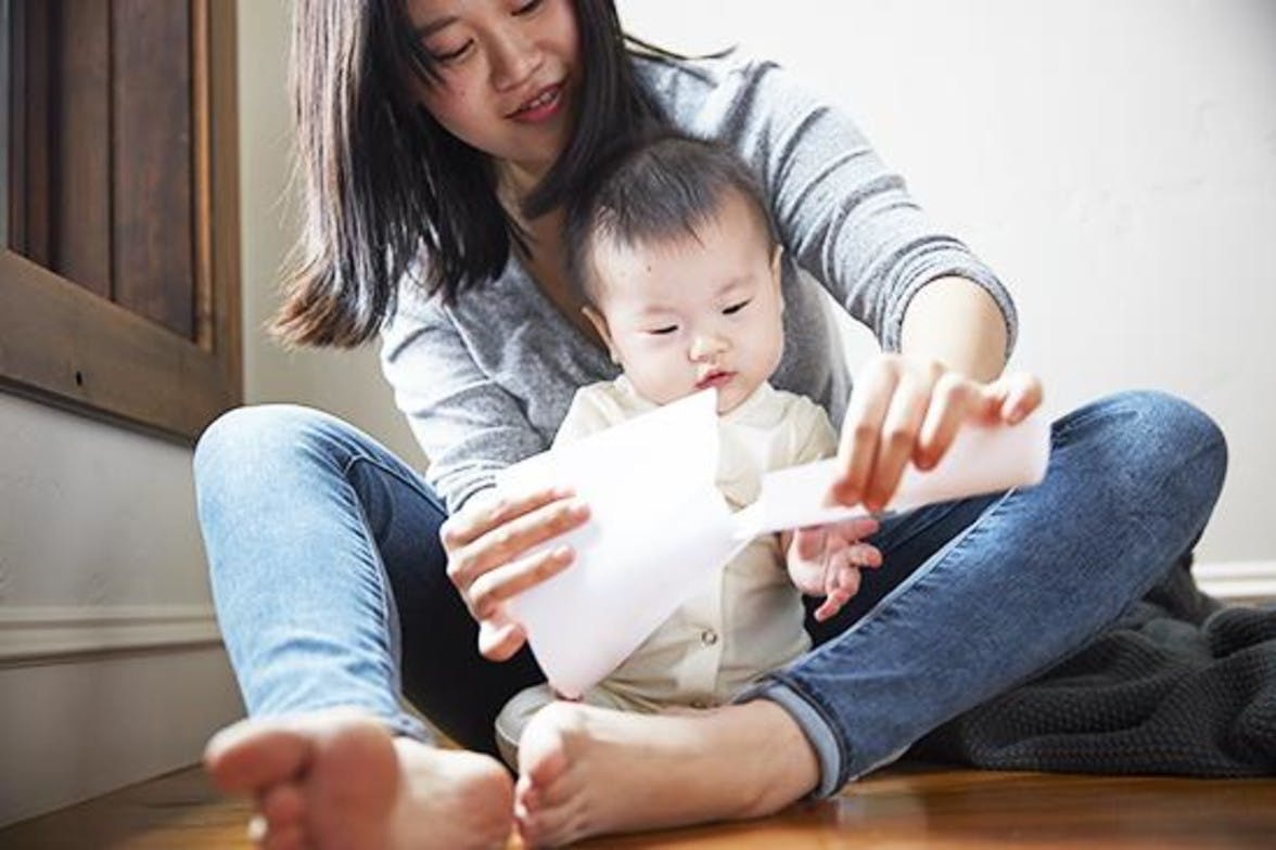 Baby sitting in front of a woman watching her rip a piece of paper