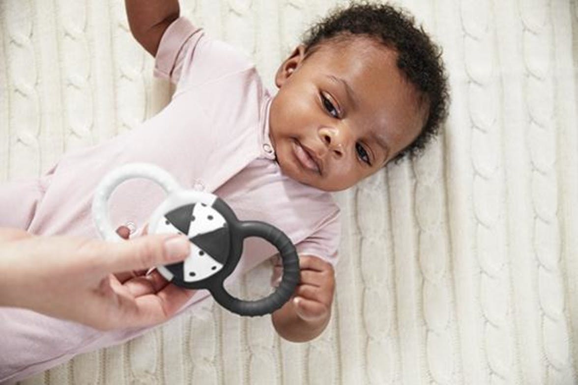 Baby laying on the ground looking up at Silicone Rattle with Removable Ball by Lovevery