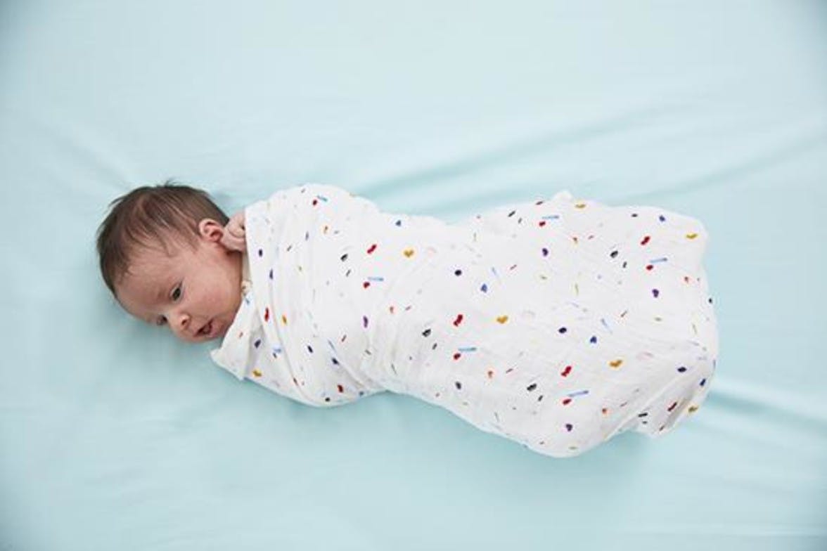 Baby laying down wrapped in an organic cotton swaddle by Lovevery
