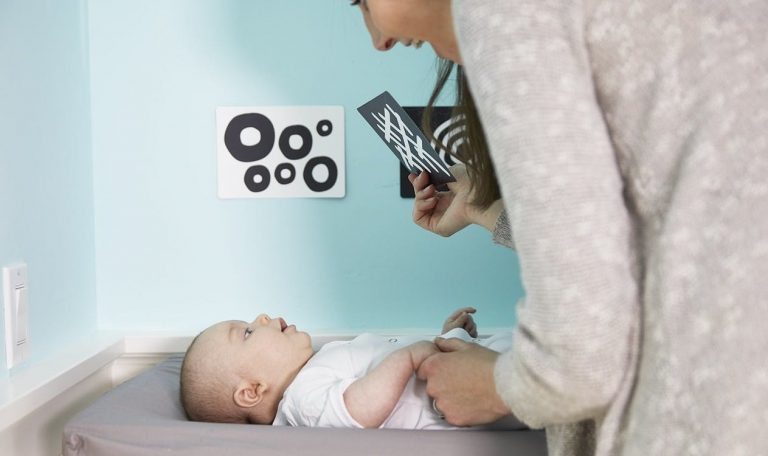 Baby laying on a changing table looking at high contrast cards held to the baby's face by a woman