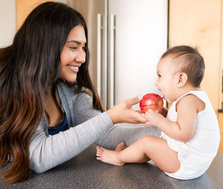 Woman helping a baby put an apple up to their mouth