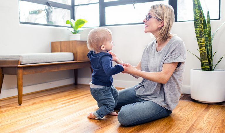 Woman holding a toddler's hand helping them to their feet