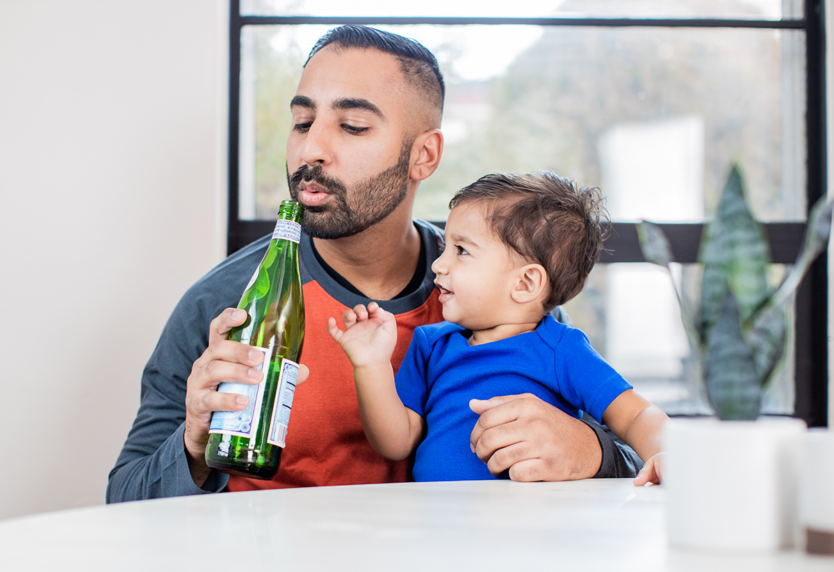 Man holding a toddler and blowing into a glass bottle to make a noise