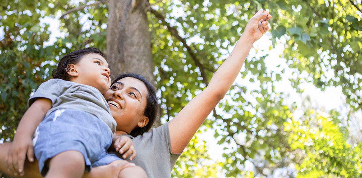 Woman holding a toddler outside pointing at the sky