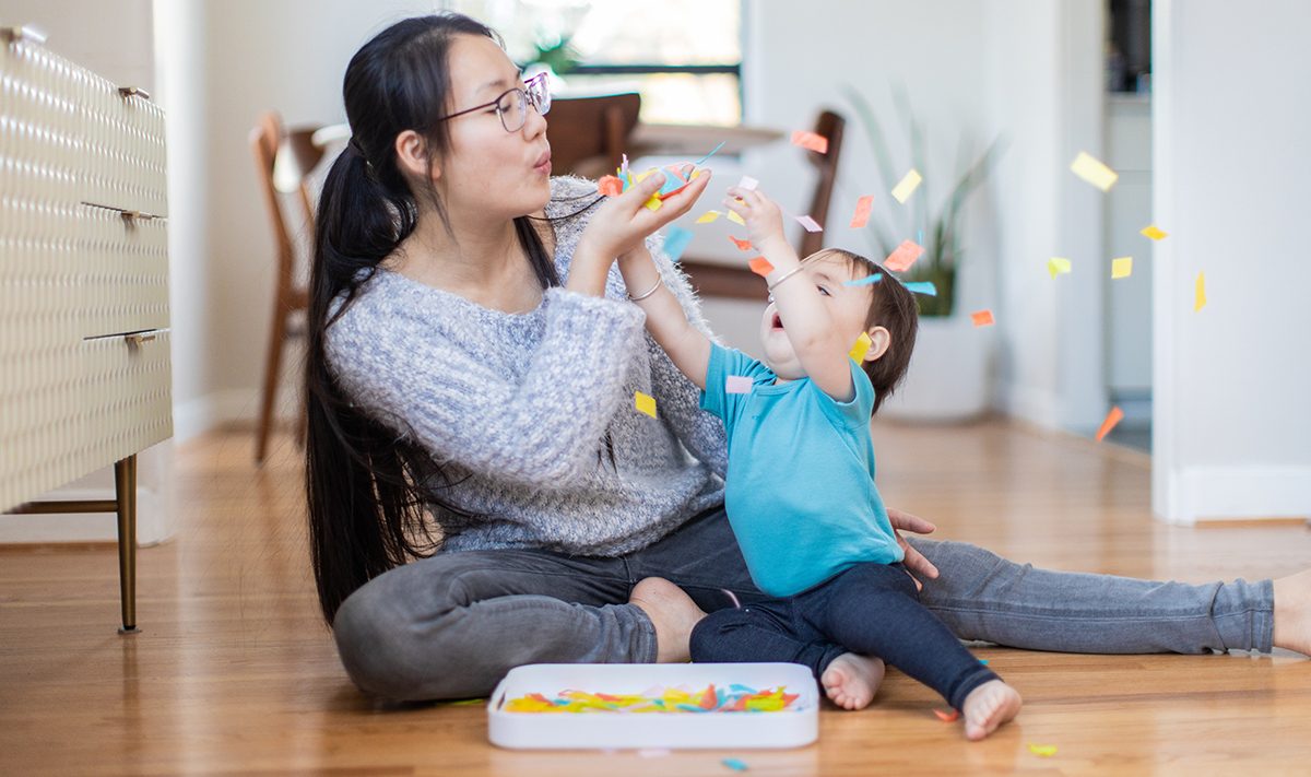 Woman blowing confetti while a toddler is reaching up at it