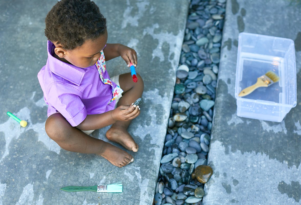 Toddler sitting outside playing with water and rocks