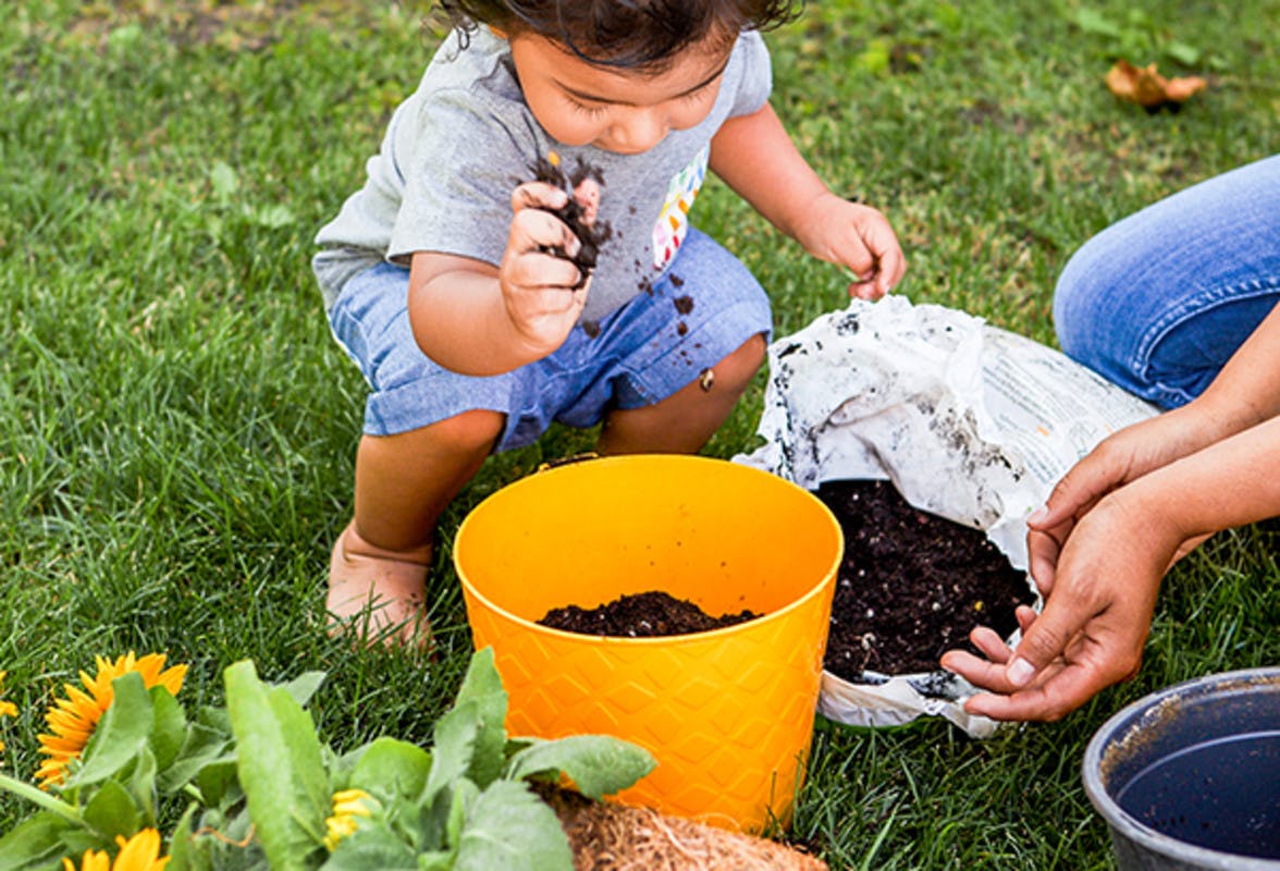 Young child outside putting dirt into an orange pot