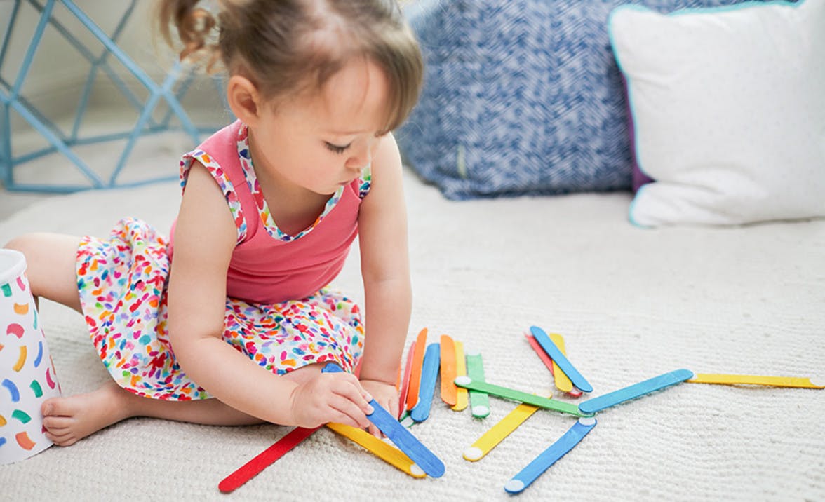 Toddler playing with colored popsicle sticks that have Velcro on the ends