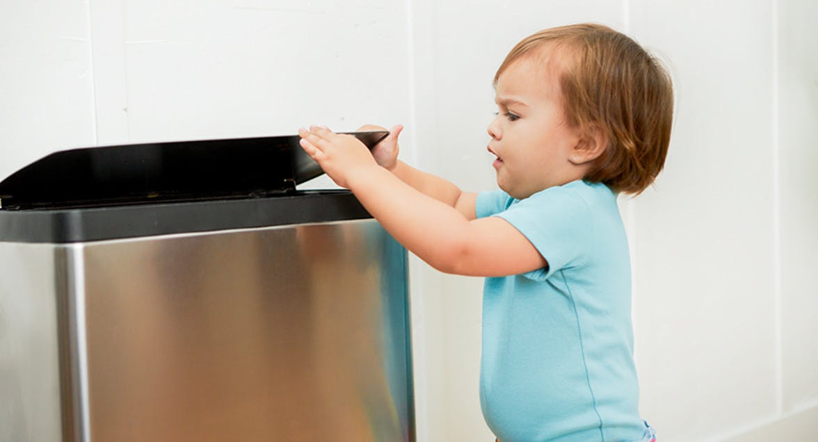 Young child closing the kitchen trashcan.