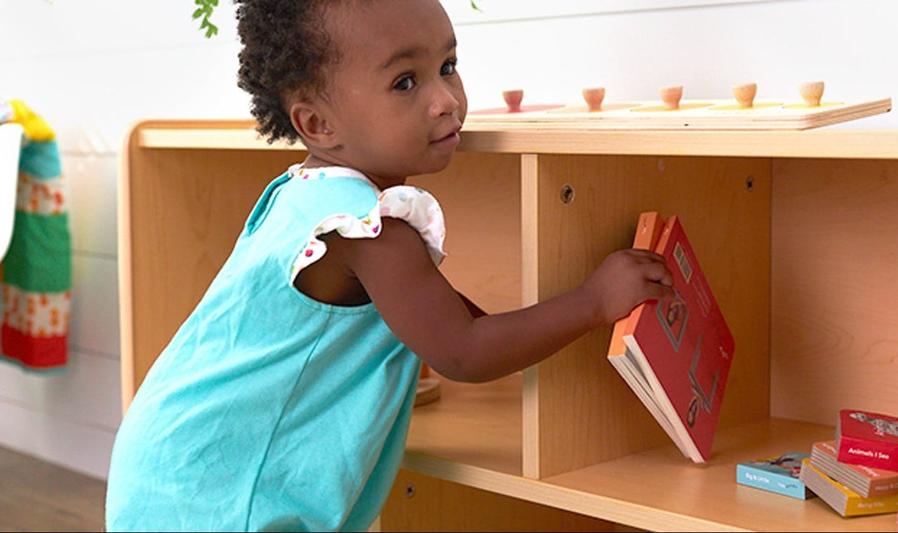 Young child putting away two books by Lovevery back on a shelf