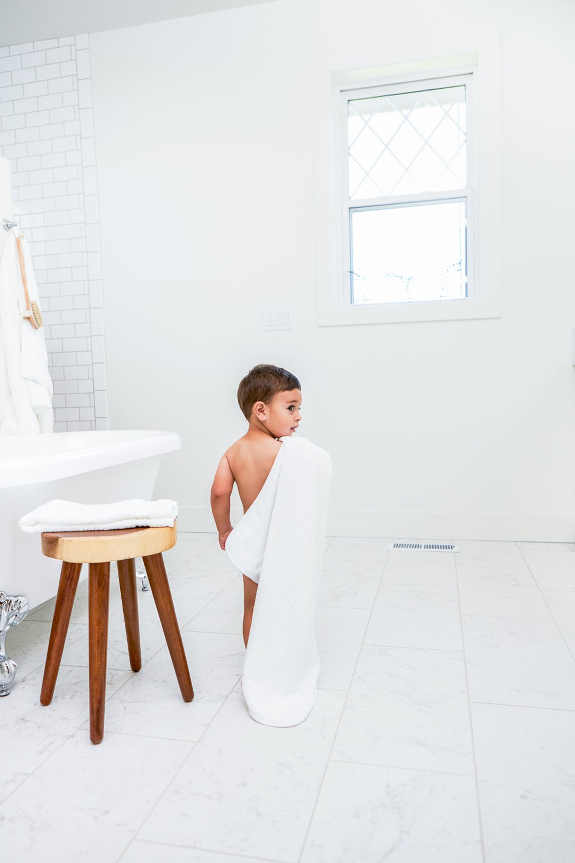 Young child holding a towel walking to a bathtub