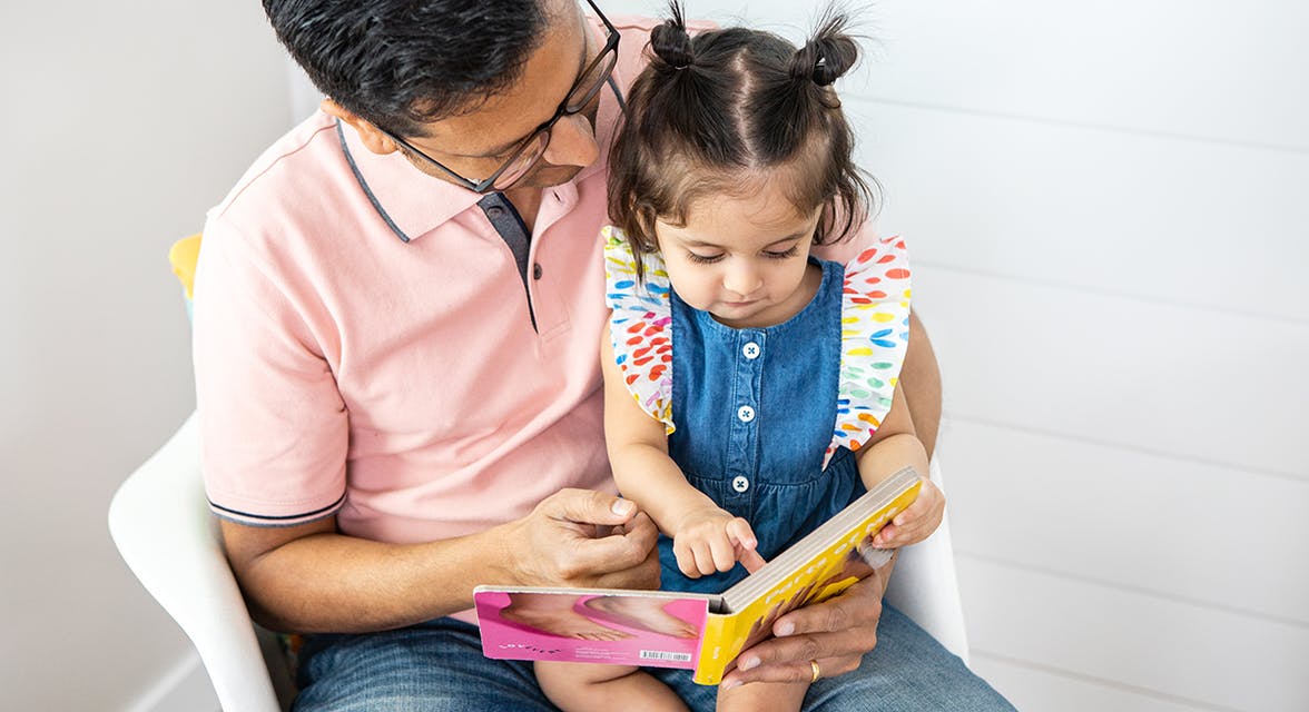Toddler sitting on a man's lap looking at a book together