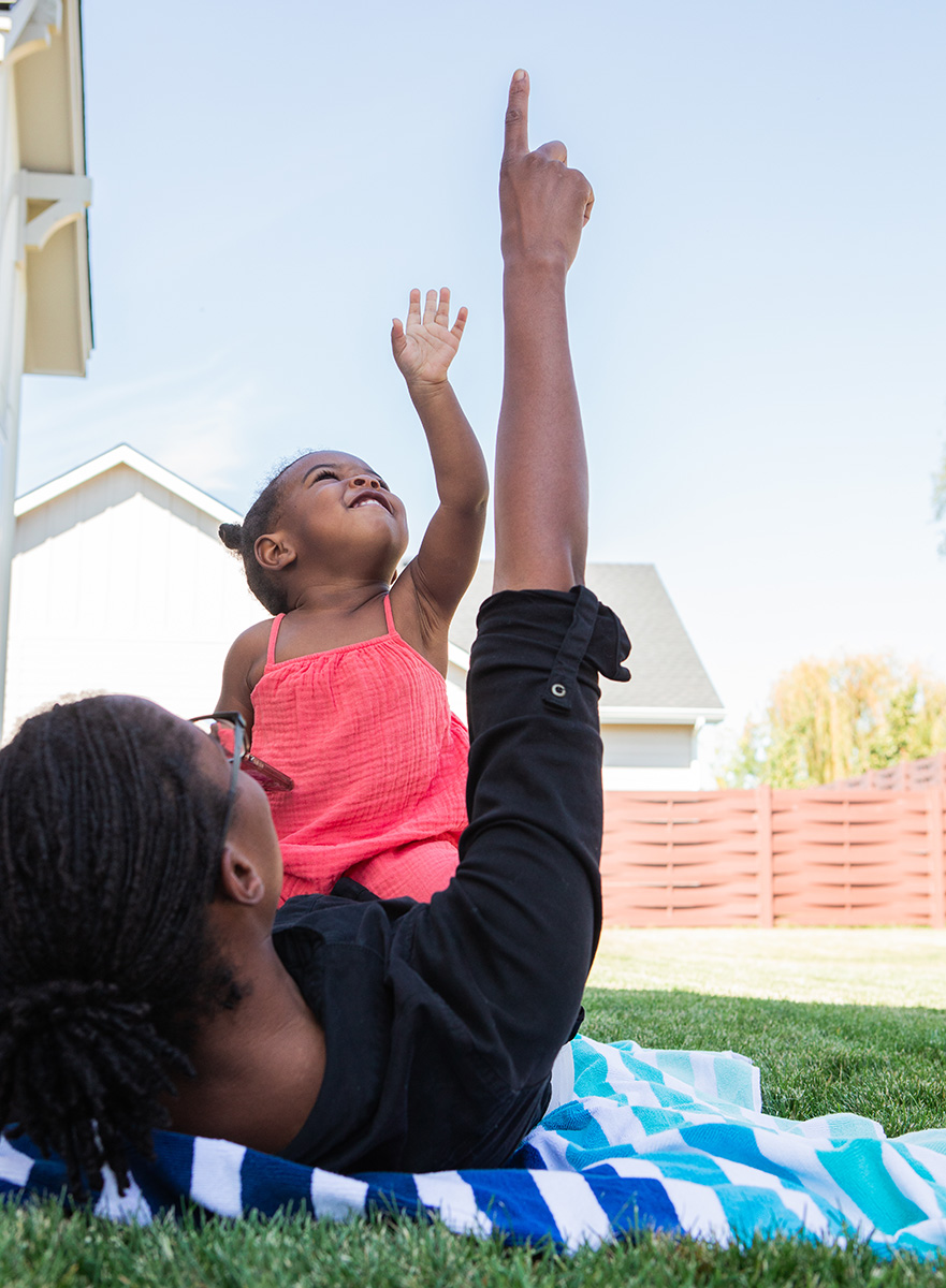 Toddler laying on a woman outside pointing up at the sky