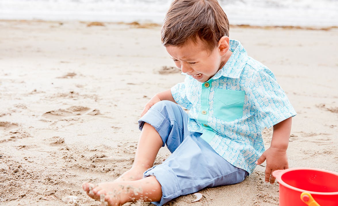 Young child crying and upset sitting in the sand at the beach