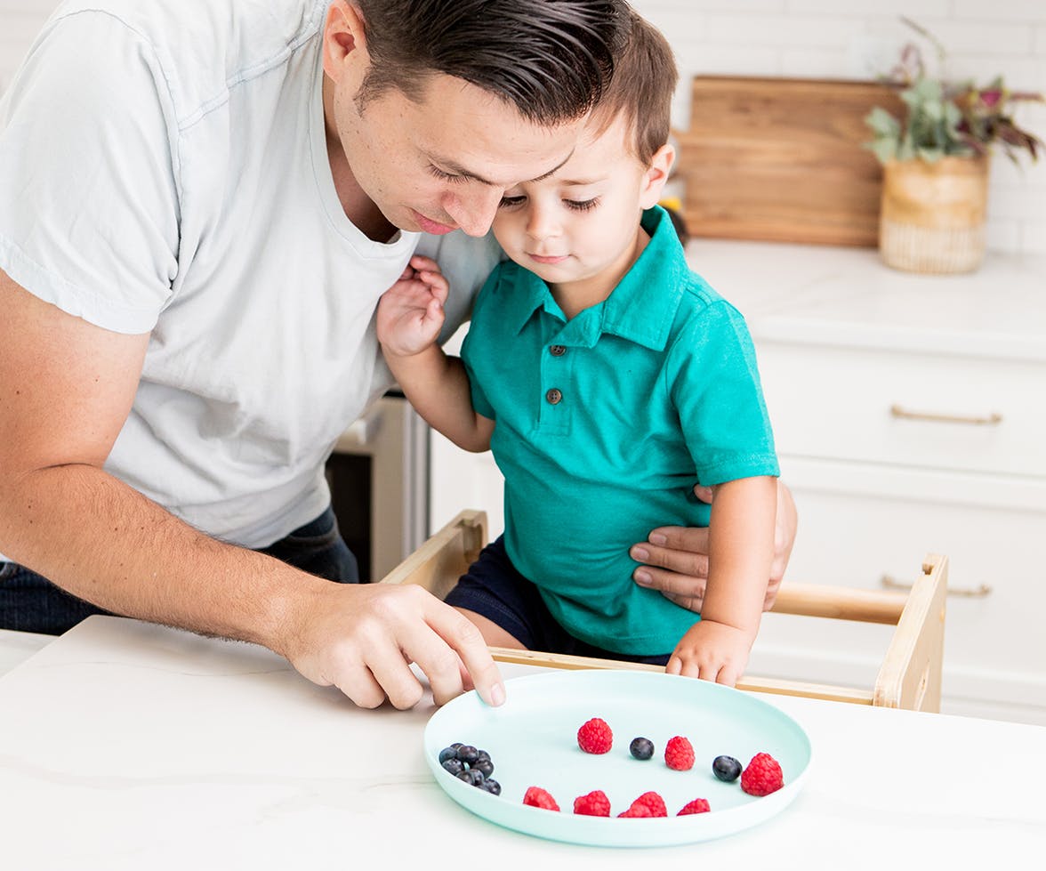 Father hugging a toddler while looking at a plate full of berries