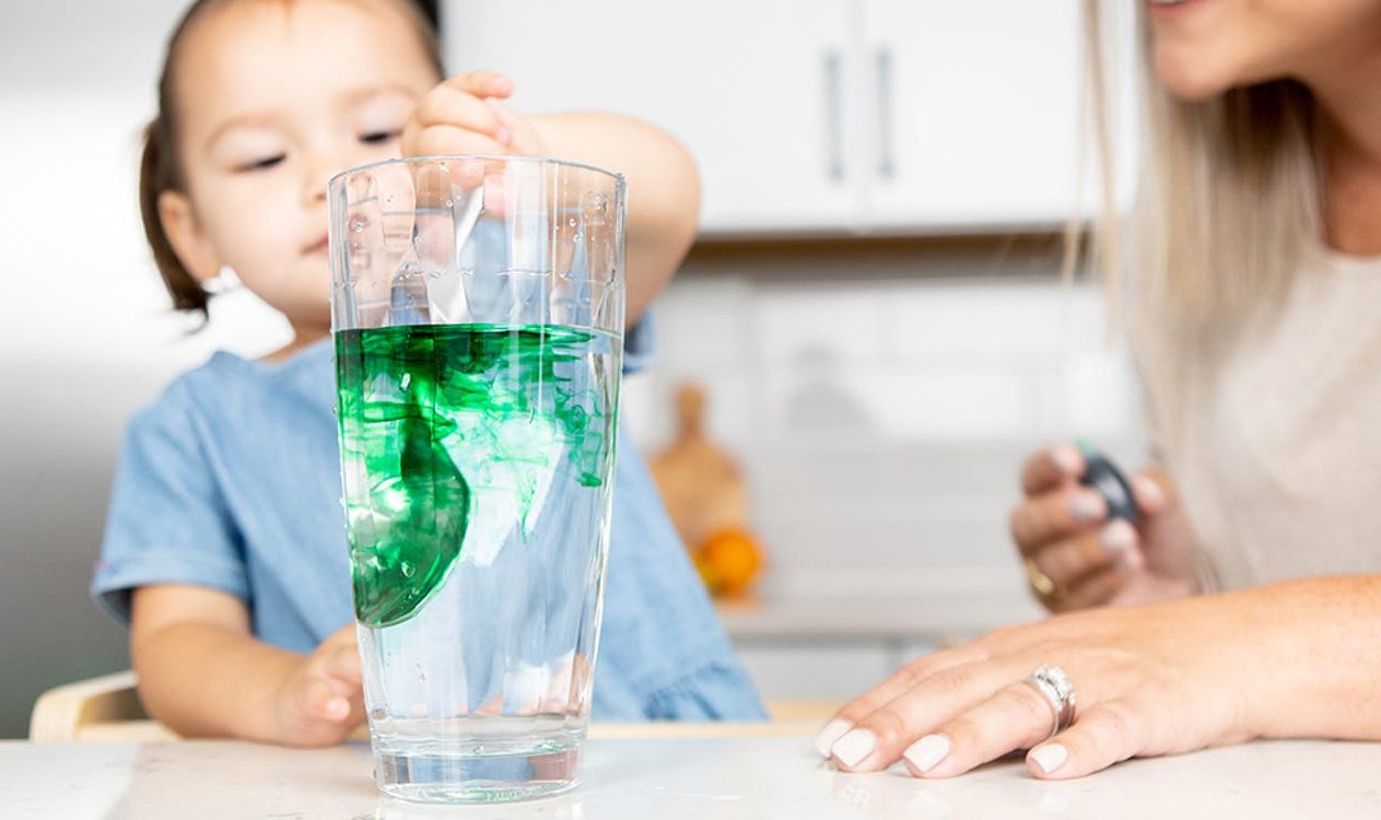 Toddler stirring green food coloring into a glass of water