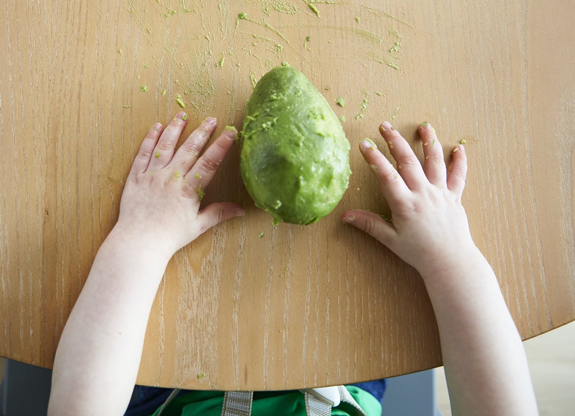A toddler's hands with a peeled avocado between them