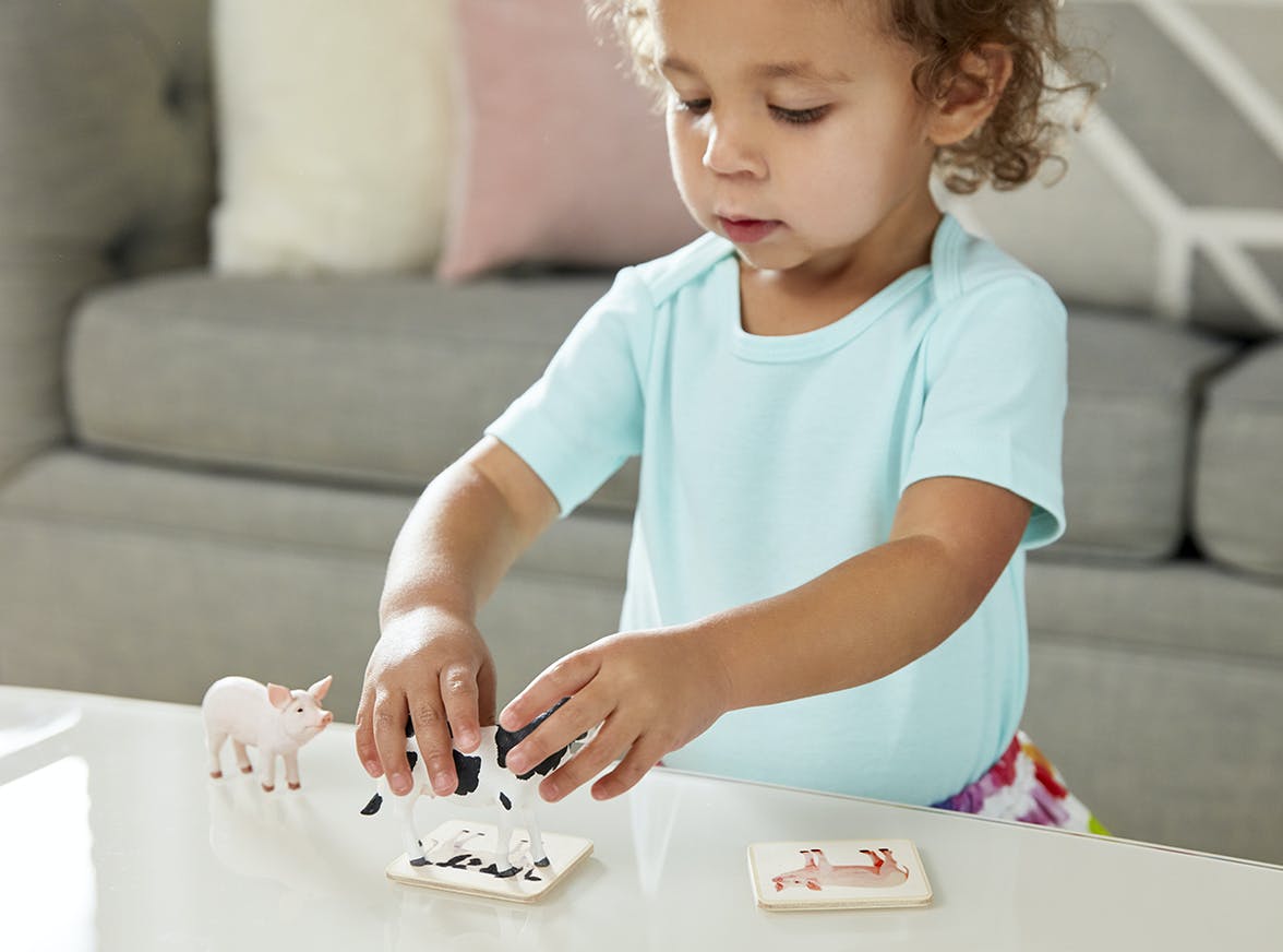 Young child holding a cow figurine on top of a wooden cow card