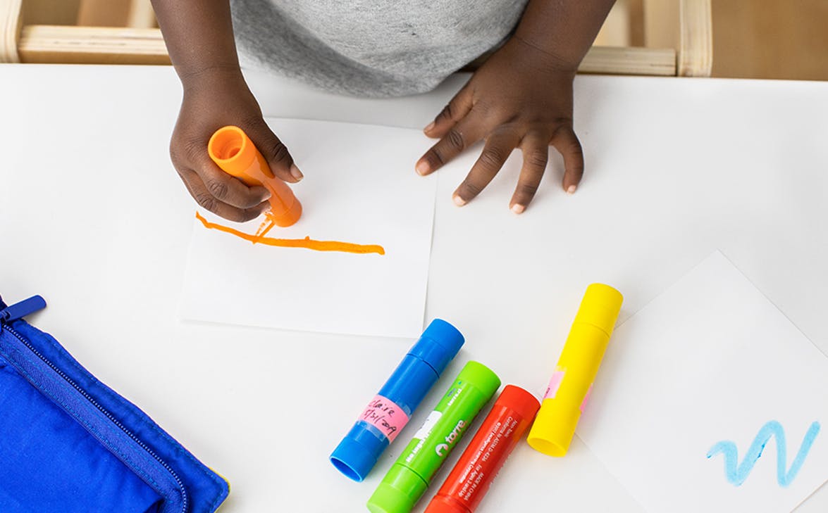 Toddler drawing on a white piece of paper with colorful markers