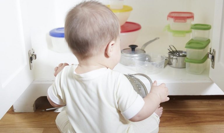 Baby sitting up and looking into an open kitchen cabinet