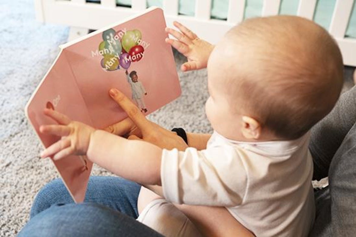 Baby sitting on a woman's lap and looking at a book by Lovevery