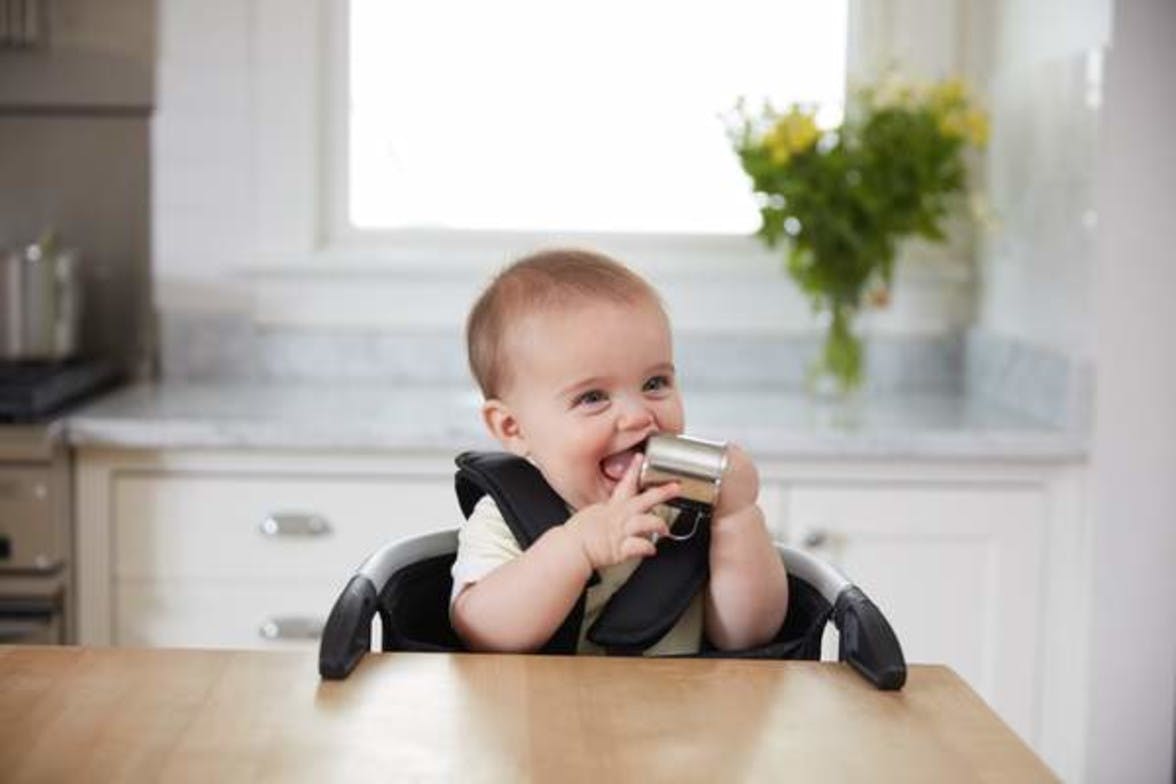 Baby sitting in a high chair holding the Drinking Cup by Lovevery