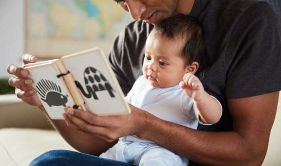 Baby sitting on man's lap looking at the Wooden Book by Lovevery