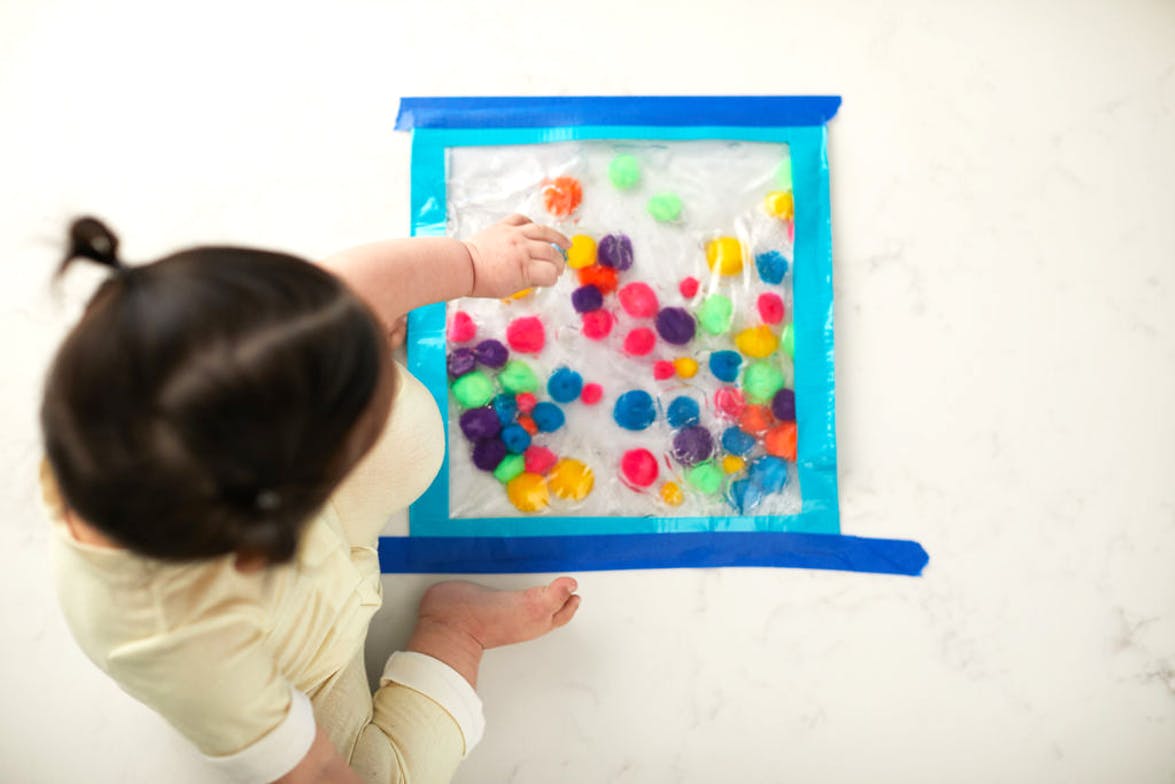 Toddler playing with a plastic bag filled with water and pom poms