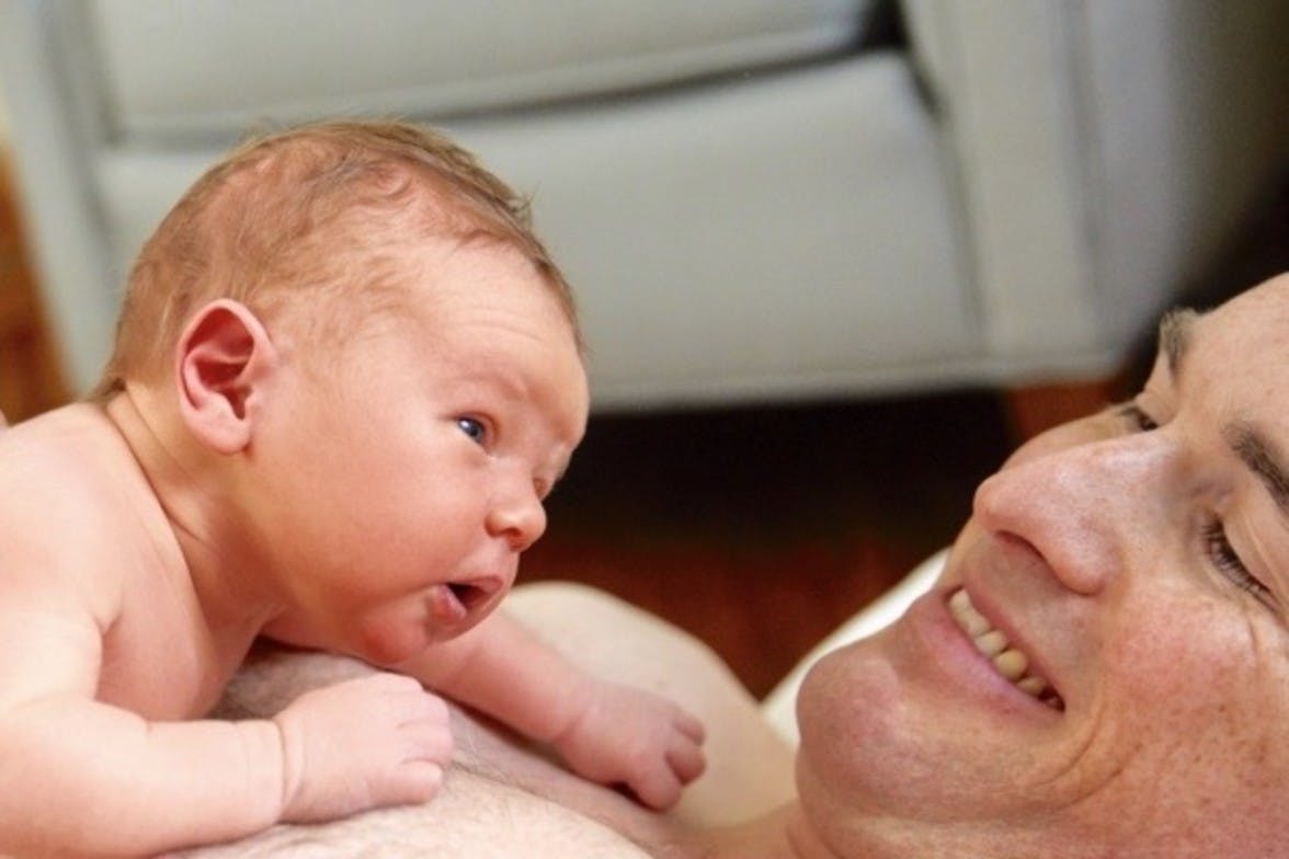 Baby laying on a man's chest doing tummy time