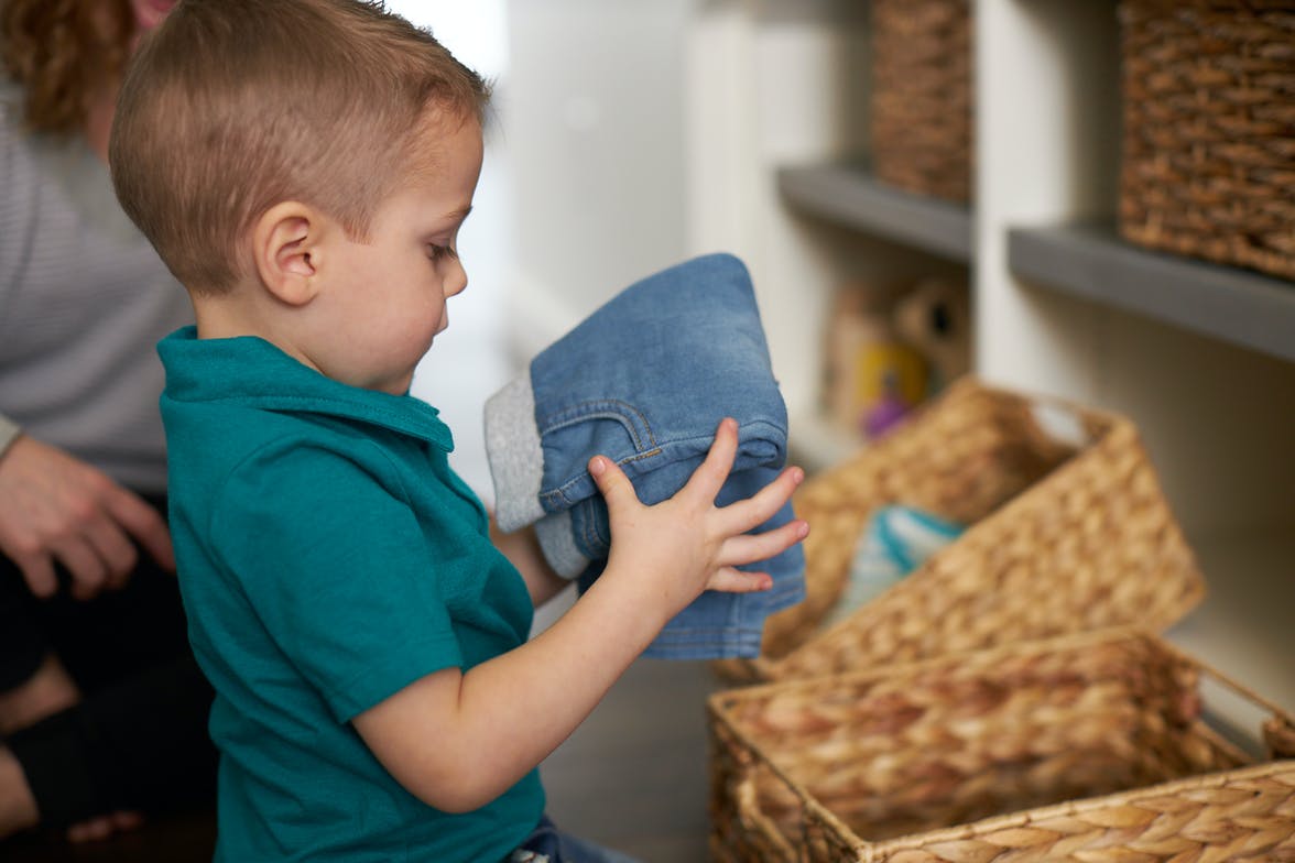 Young child putting folded jeans into a basket