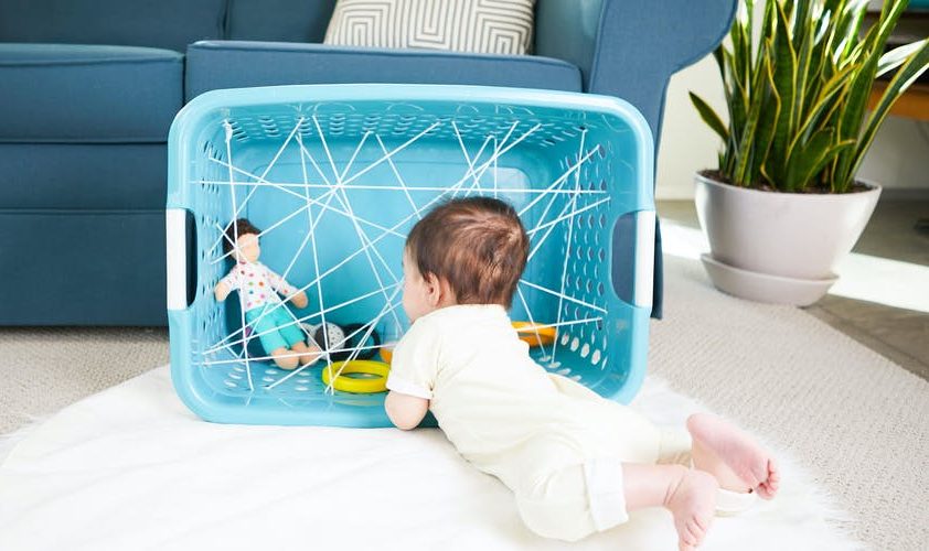Baby laying on their stomach looking at a laundry basket with their toys inside