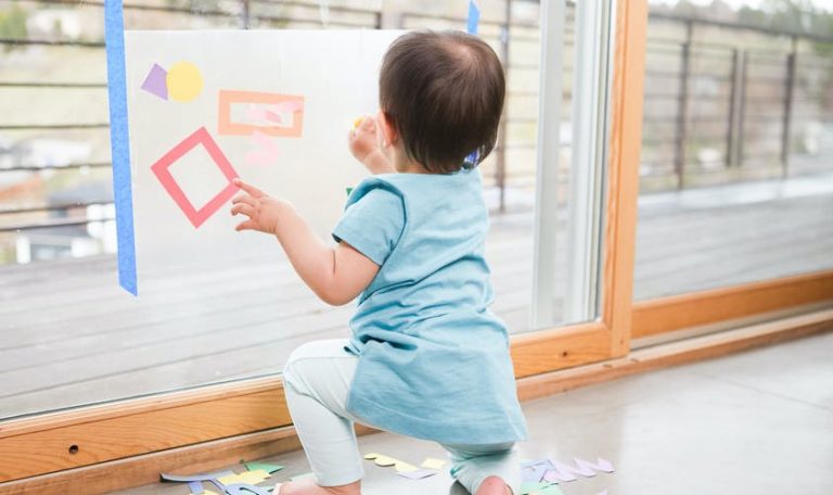 Baby playing with contact paper that's attached to a glass door