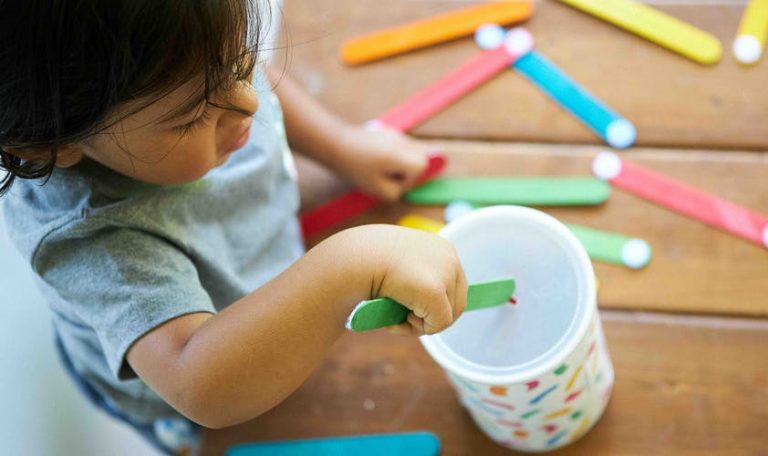 Toddler putting a popsicle stick into a container