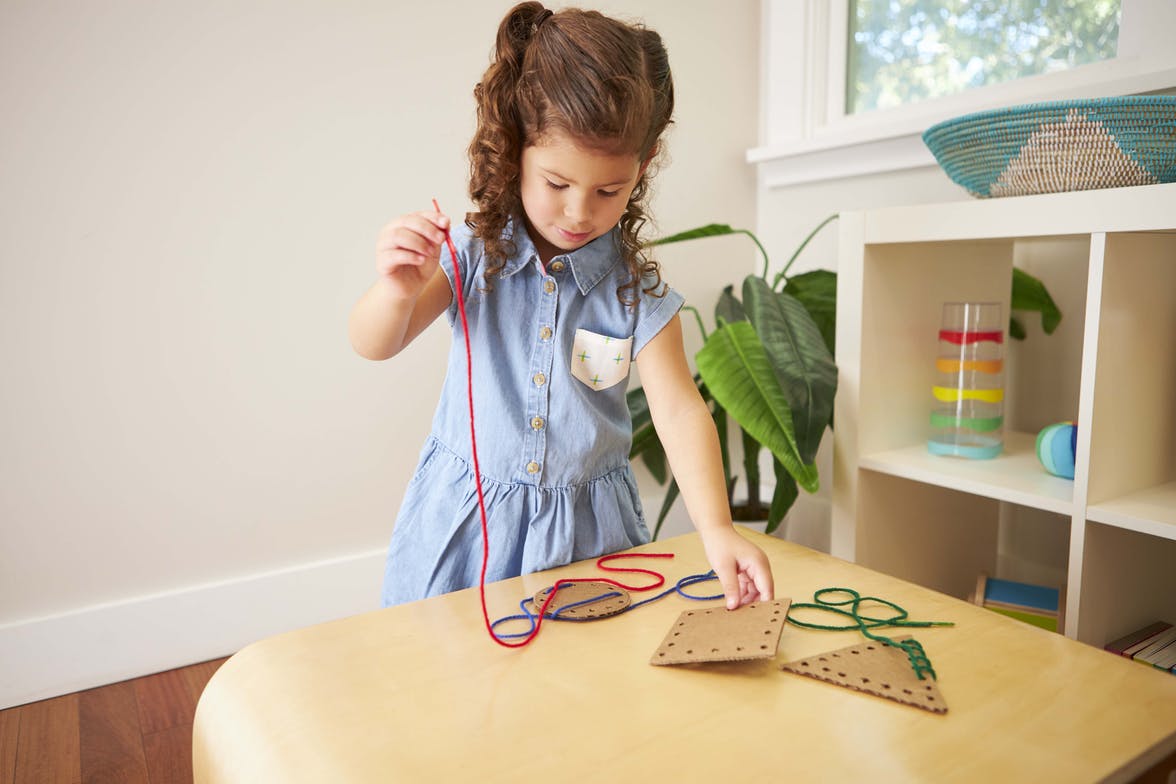 Young child stringing yarn through cardboard