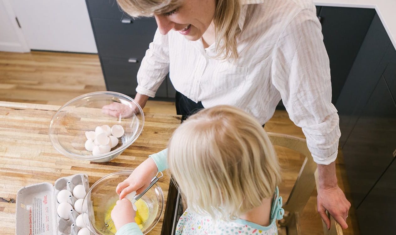 Toddler cracking an egg into a mixing bowl in the kitchen