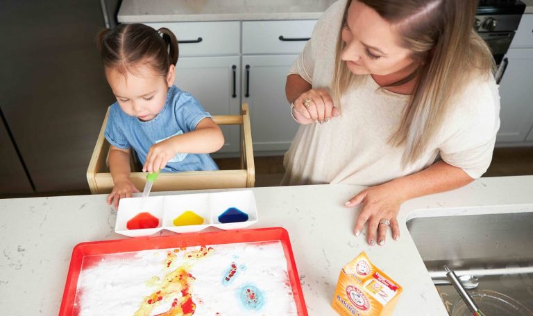 Toddler doing a STEM activity with baking soda, food coloring, and water