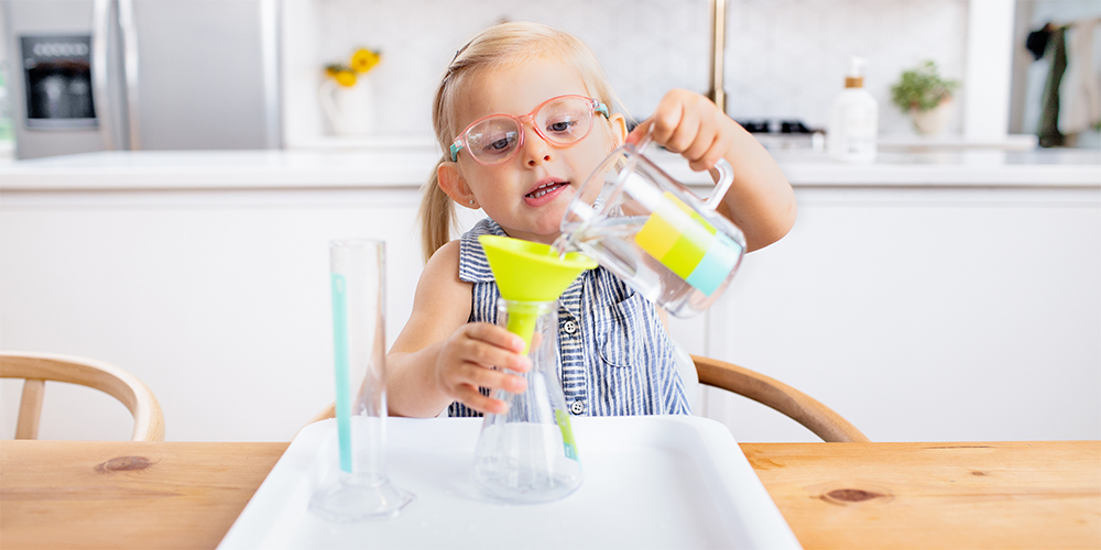Young child pouring liquid into a funnel at the kitchen table