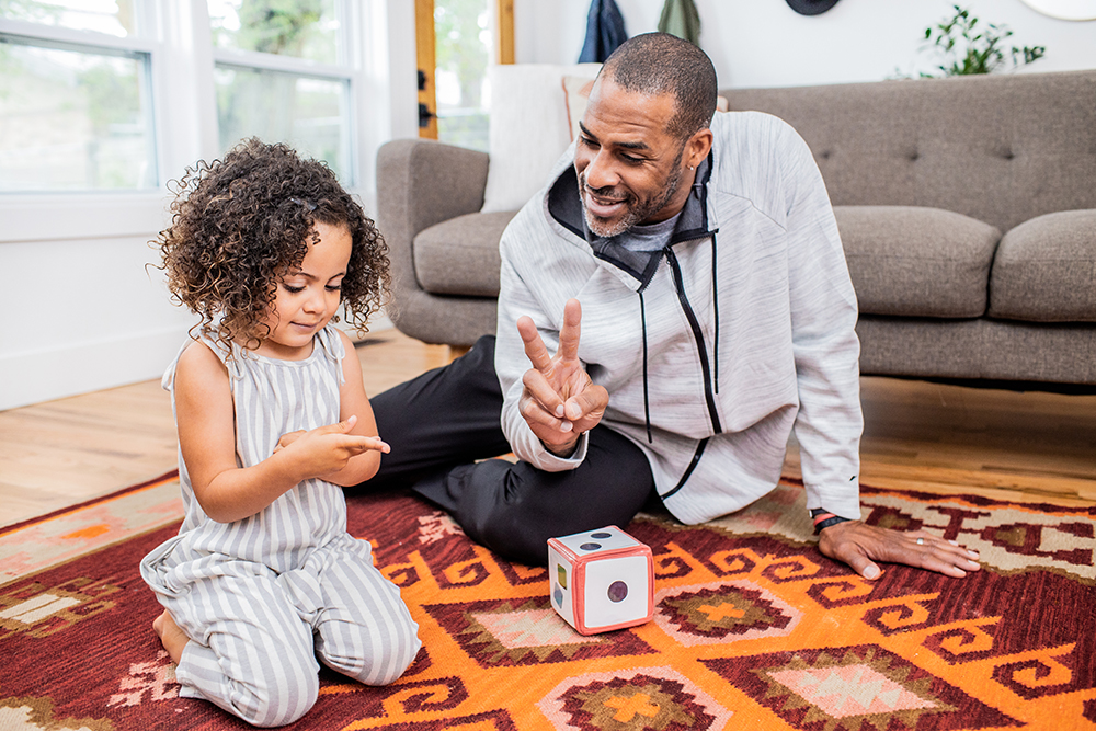 Young child and man sitting on the floor holding up two fingers