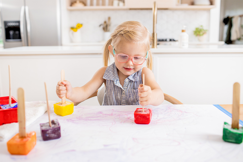 Toddler sitting at a table playing with colored ice on a piece of paper