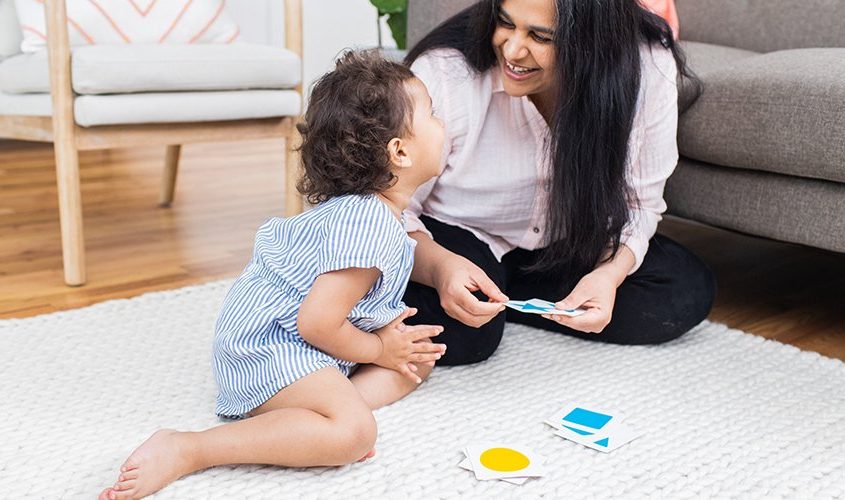 Young child smiling at a woman as they look through cards of shapes and colors