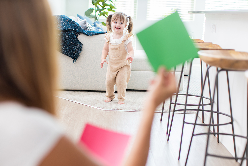 Toddler walking while a woman is holding up a green card