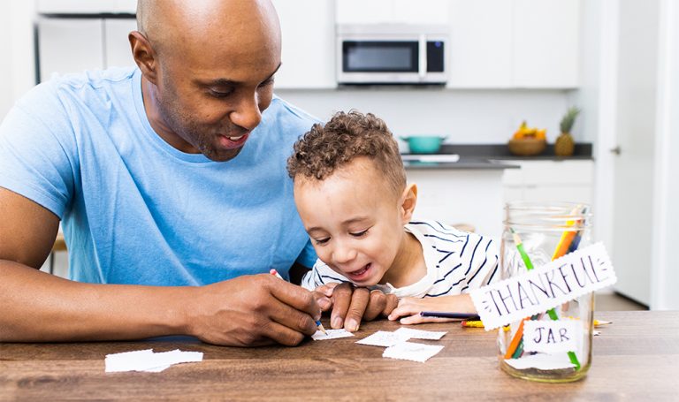 Young child sitting with a man writing things down on paper