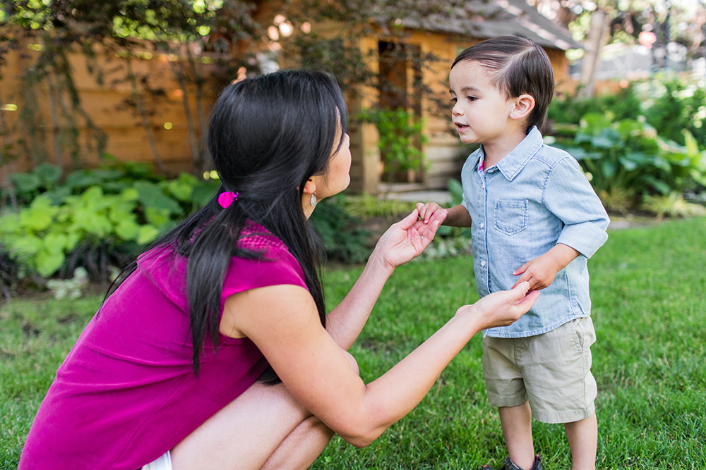 Woman holding hands with a toddler while standing outside in the grass