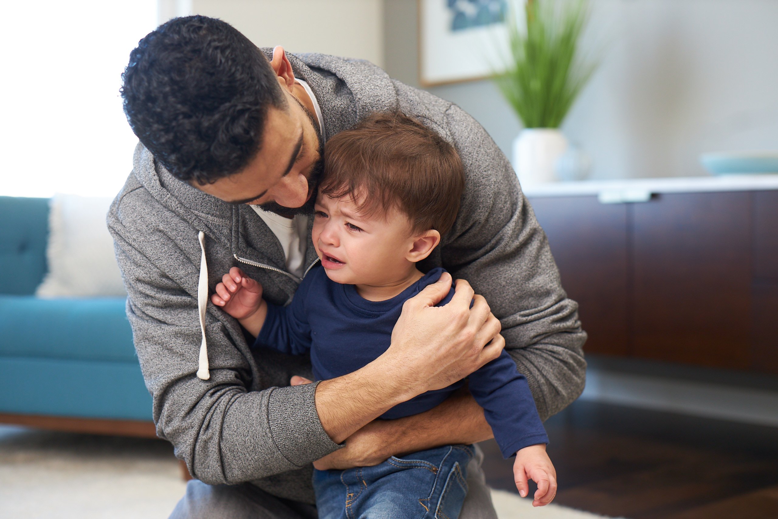 Man hugging an upset toddler from behind