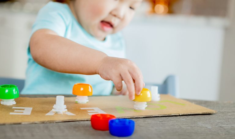 Toddler screwing on a pouch top attached to cardboard