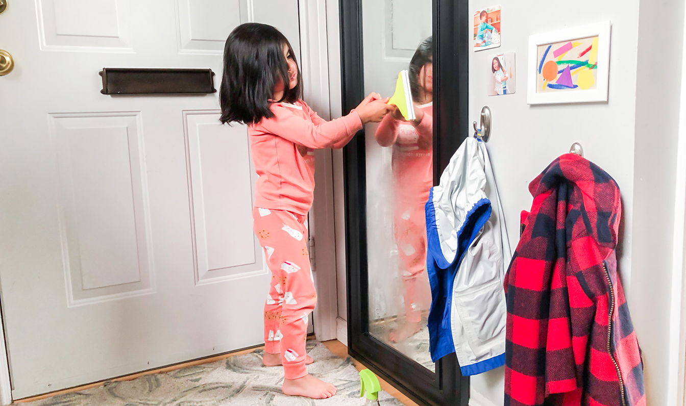 Young child cleaning a window with the Squeaky Clean Squeegee Set by Lovevery