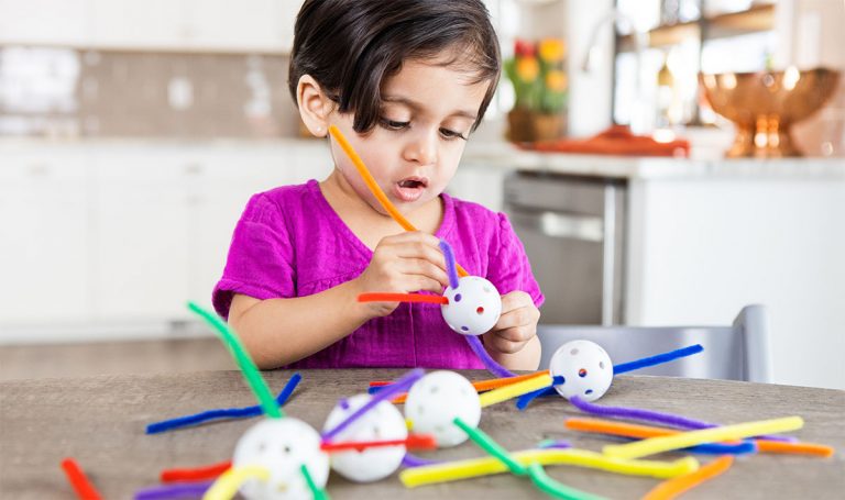 Toddler putting pipe cleaners through a whiffle ball