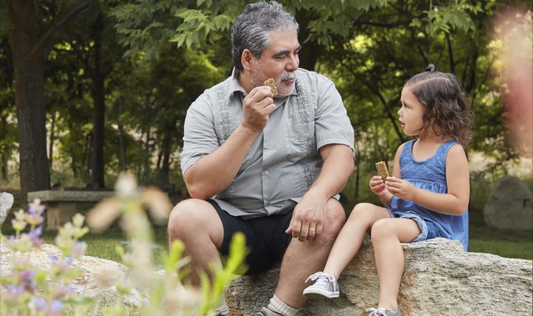 A young child an man sitting on a rock eating a snack